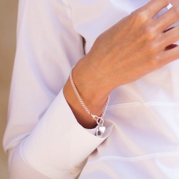 Model wearing designer heavy solid silver chain horseshoe and heart bracelet on white background. 
