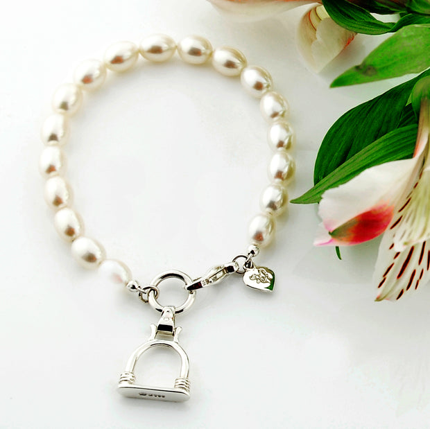 designer silver and cultured pearl bracelet with vintage stirrup charm on white background with flower.