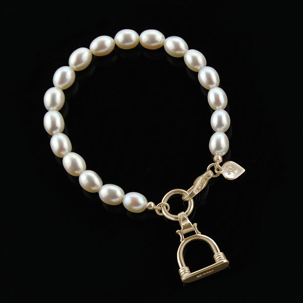designer solid gold stirrup and cultured pearl bracelet on a black background.