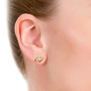 close up of model wearing designer gold knotted strap stud earrings on white background.
