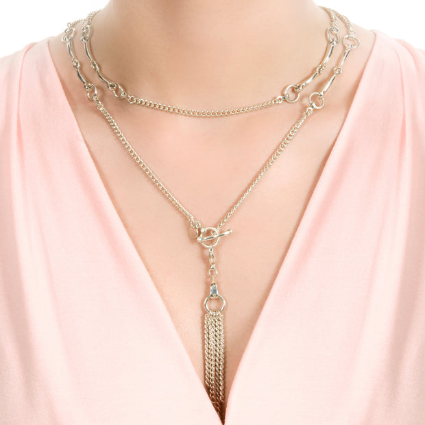 neck shot of model wearing designer silver lariat equestrian bit and chain necklace with chain tassel on white background