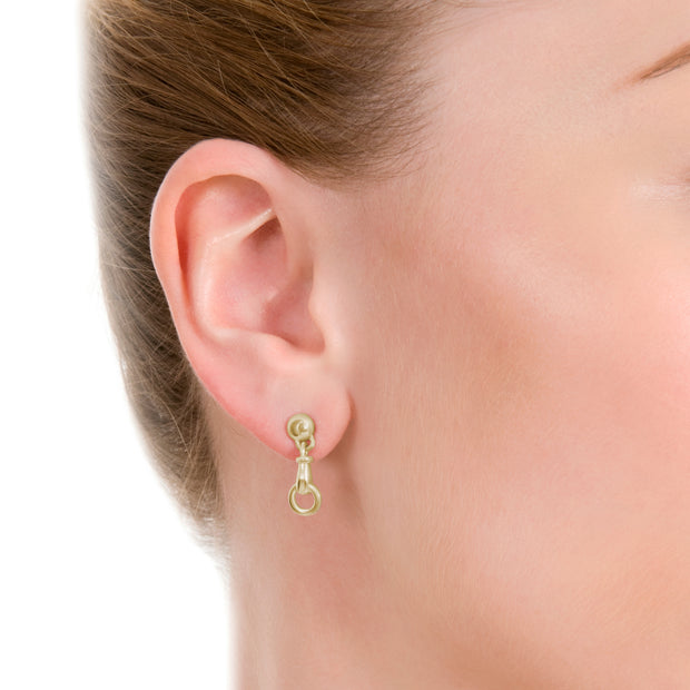 close up image of model wearing designer solid 9ct yellow gold horse bit inspired drop earrings on white background.