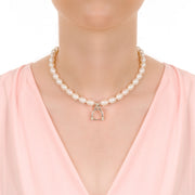 close up of model's neck wearing designer cultured pearl necklace with vintage solid silver stirrup design charm on white background.