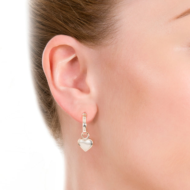 ear shot of model wearing designer solid silver leather strap hoops with removable heart drop earrings on white background.