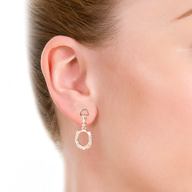 close up shot of model wearing designer solid silver horseshoe drop earrings with bit top detail on white background